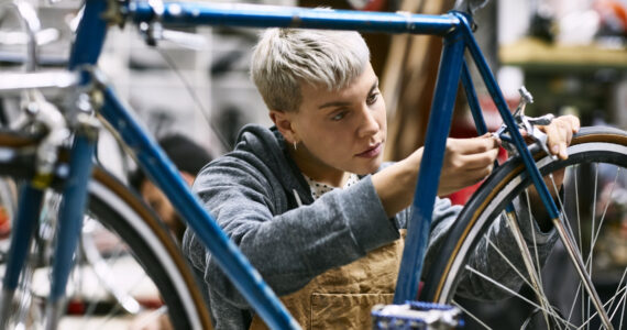 Young female mechanic repairing bicycle brake at workshop. Confident employee is working at repair shop. She is wearing apron.